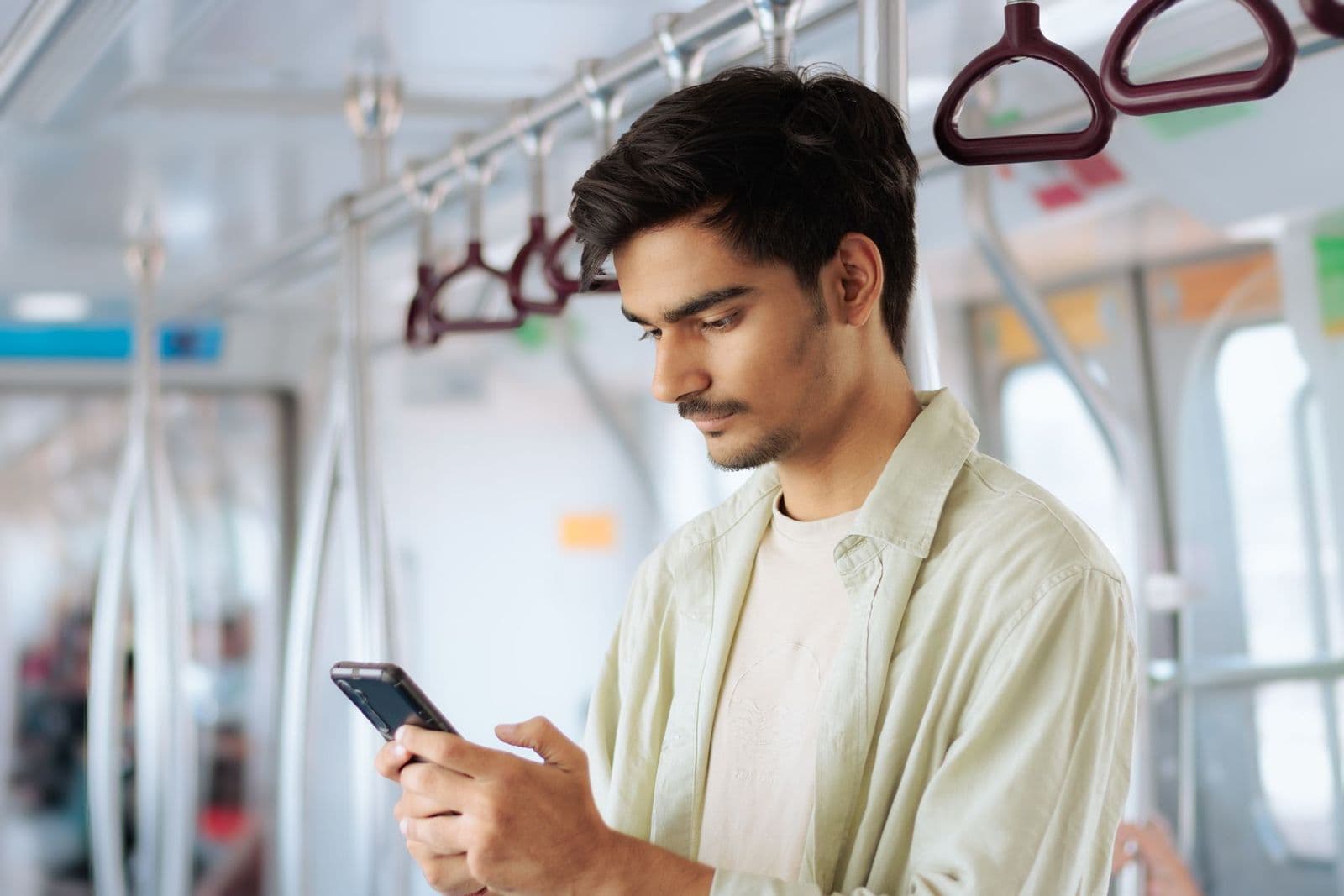 A young man in a light shirt looks at his smartphone while standing in a metro train carriage